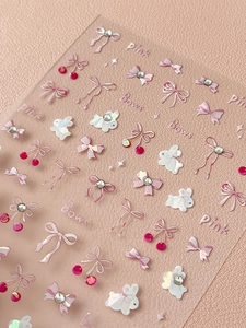 Macro detail of 3D pink bow and rabbit nail art stickers with iridescent finish