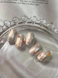 Macro detail of floral nail art stickers with dried flowers and gold foil on pink base