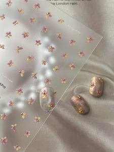 Macro detail of 3D pink and yellow floral nail art stickers with gold bead accents