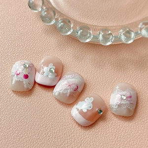Pink and white press-on nails with 3D bunny, bows, lace patterns and rhinestones