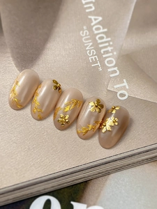 Detail of nude pink press-on nails with 3D gold floral accents and leaf patterns