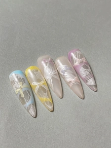 Detailed view of handmade press-on nails with 3D bows, pearls, and white lace textures
