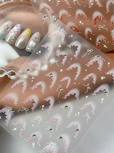 Dettaglio di adesivi per unghie con fiocchi bianchi, sfumature rosa e strass lucenti