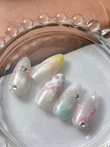 Dettaglio di unghie a mandorla macaron con perle e strass su un vassoio di vetro