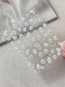 Makroaufnahme von weißen 3D-Präge-Nagelstickern mit Perlendetails und orangefarbenen Akzenten