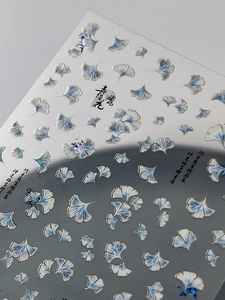 Macro detail of silver and blue ginkgo leaf nail stickers with metallic embossed texture