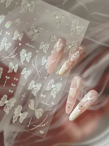 Détail de stickers 3D blancs à nœuds papillon avec perles sur ongles dégradés roses