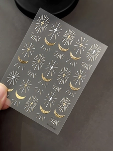 Detailed view of silver and gold cross and crescent moon nail art stickers on dark background