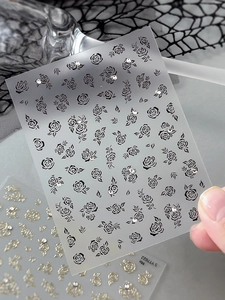 Close-up of black and white rose nail stickers with sparkling rhinestones and gold details