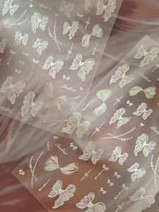 Détail d'autocollants nail art 3D blancs avec nœuds, chaînes de perles et effet laser