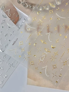 Dettaglio di adesivi per unghie oro e argento con motivi di sole luna e stelle metalliche