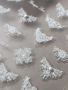Detailed macro view of silver embossed lace nail art sticker with tiny pearl accents