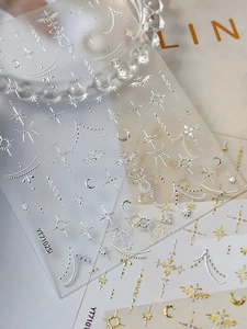 Dettaglio macro di adesivi per unghie oro e argento con motivi luna, stelle e texture a rilievo