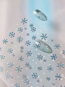Close-up of metallic blue and silver snowflake nail stickers on light blue base nails