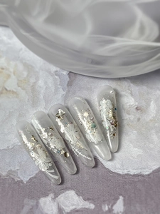 Dettaglio di unghie finte bianche opache con rilievi floreali 3D e perle eleganti