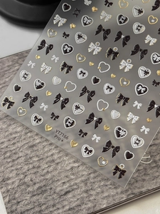 Macro shot of 3D embossed bow and heart nail stickers with gold foil on grey texture