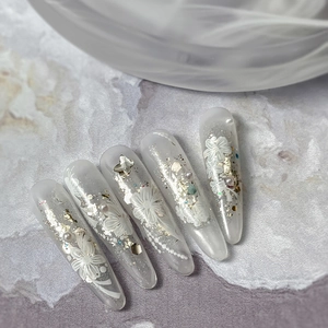 Unghie finte stiletto lunghe ed eleganti con trame floreali bianche e perle applicate