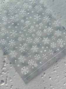 Close-up of white embossed snowflake nail art stickers with 3D texture and stars