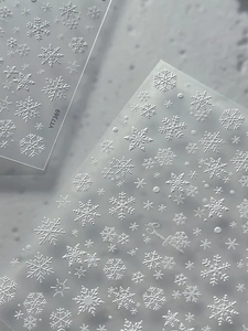 Macro detail of 5D embossed white snowflake nail stickers with textured winter patterns
