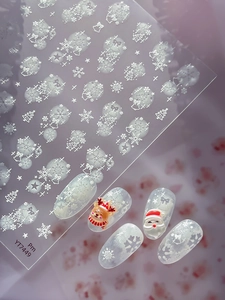 Dettaglio di adesivi per unghie natalizi con fiocchi di neve bianchi e decori Babbo Natale