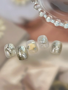 Detail of luxury press-on nails with pearl finish, metallic hearts and cross charms