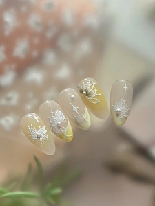Detailed view of yellow almond press-on nails with white butterfly and pearl accents