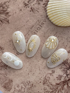 Close-up of handmade press-on nails with shell texture and gold 3D celestial patterns
