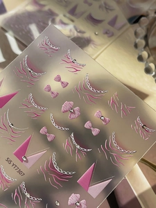 Macro shot of pink bow nail stickers with rhinestone accents and silver chain patterns