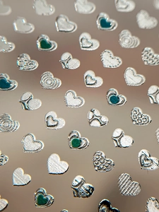 Macro view of 3D silver heart nail art stickers with embossed textures and green accents