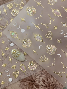 Macro detail of gold embossed nail stickers with sparkling shell and celestial patterns