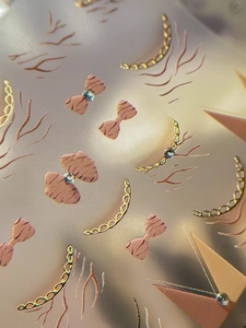 Macro detail of French nail art stickers featuring 3D rhinestone bows and gold chain patterns