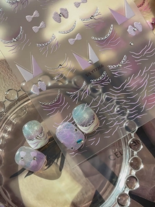 Close-up of 3D embossed nail art stickers featuring purple bows and silver pearls