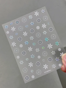 Macro detail of holographic silver laser snowflake nail stickers with blue metal accents