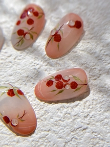 Macro detail of peach almond nail stickers with red berry designs and 3D water drops