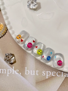 Detail of silver glitter press-on nails with cartoon eyes and colorful patterns