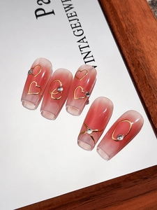 Detail of red gradient press-on nails with gold heart patterns and rhinestone inlay