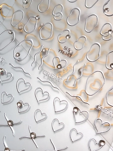 Macro shot of 3D embossed silver nail art stickers with heart shapes and sparkling rhinestones