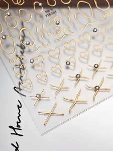 Macro shot of 3D gold heart nail stickers with rhinestones and metallic wavy lines