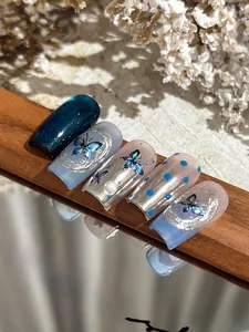 Detail of laser silver and blue butterfly nail art stickers with pearl accents on wood
