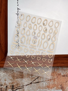 Close-up of gold heart and geometric nail stickers with rhinestones on transparent sheet