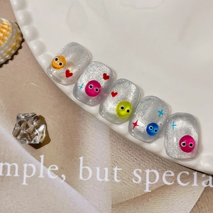 Silver cat eye press-on nails with 3D cartoon smile faces and glitter stars on white plate