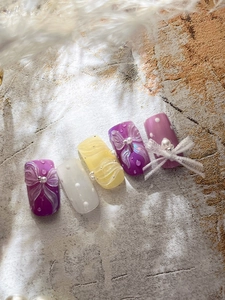 Detailed view of lilac and cream bow nail art with pearl accents and 3D textures