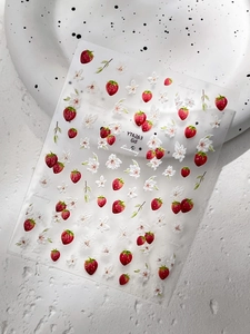 Gros plan d'autocollants pour ongles fraises et fleurs sur une surface blanche texturée