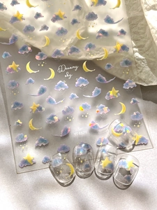 Close-up of holographic nail stickers with dreamy cloud and moon patterns on a sample nail