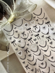 Detail view of lace French nail stickers featuring black bows and heart frame patterns