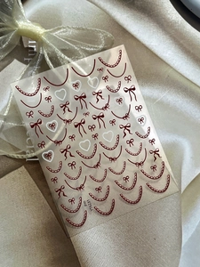 Close-up of lace nail stickers with red bows and pearls on champagne satin fabric