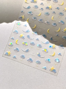 Macro detail of laser holographic nail stickers with dreamy blue clouds and yellow moon