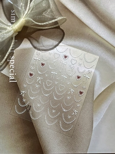 Detail of white lace and red bow nail stickers on elegant champagne satin fabric