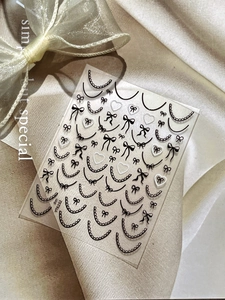 Lace French nail art stickers featuring black bows and white hearts on beige fabric