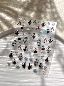 Detailed view of black swan nail art stickers with glitter effects on a ceramic plate